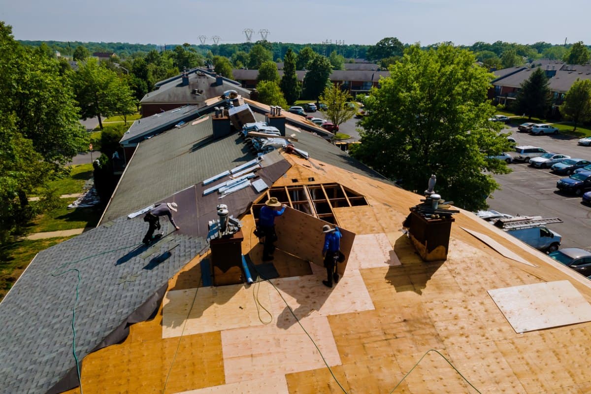 Aerial view of roofers replacing shingles and plywood sheathing on an apartment building